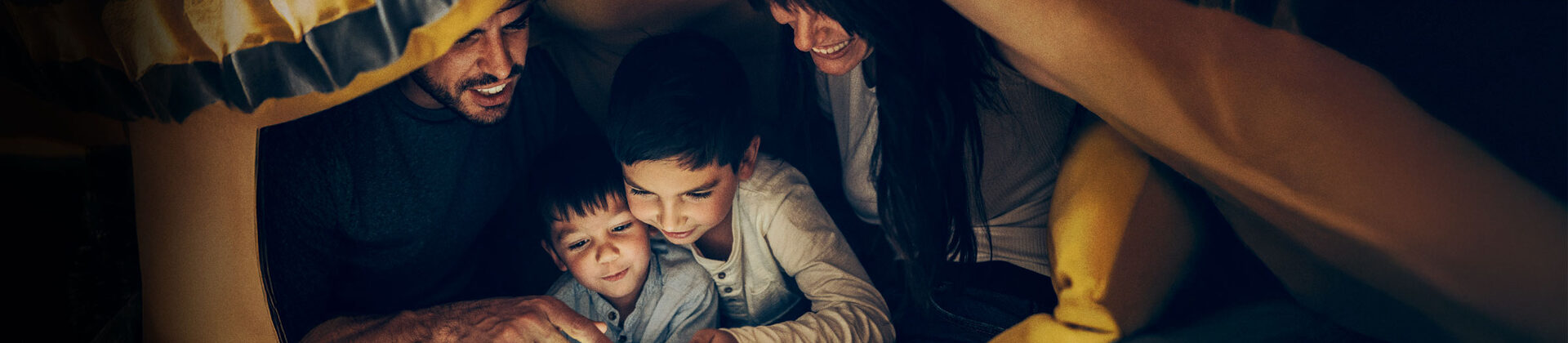 Eine Frau und ein Mann lesen mit ihren beiden Kindern unter einem Zelt.