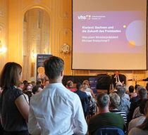 vhs-Veranstaltung in einem Stuckverzierten Saal mit dem sächsischen Ministerpräsidenten Michael Kretschmer auf dem Podium, im Vordergrund Zuschauer
