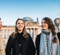 Drei junge Menschen stehen vor dem Reichtstag in Berlin. Die Stimmung ist fröhlich.