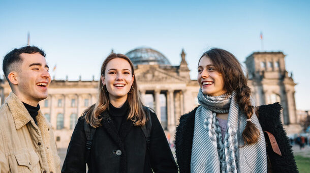 Drei junge Menschen stehen vor dem Reichtstag in Berlin. Die Stimmung ist fröhlich.