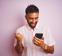Junger Mann freut sich über Nachricht am Smartphone.