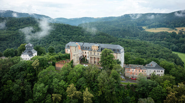 Ansicht der Schloss Schwarzburg in Thüringen aus der Luftperspektive. Das Schloss liegt auf einer Anhöhe und ist von einem Wald umgeben.