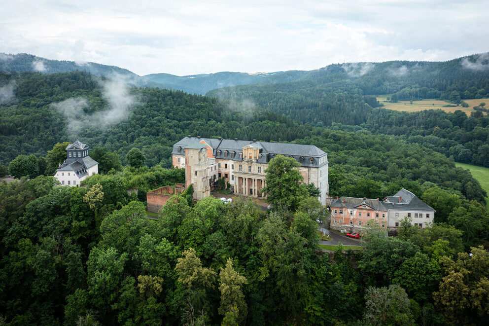 Ansicht der Schloss Schwarzburg in Thüringen aus der Luftperspektive. Das Schloss liegt auf einer Anhöhe und ist von einem Wald umgeben.