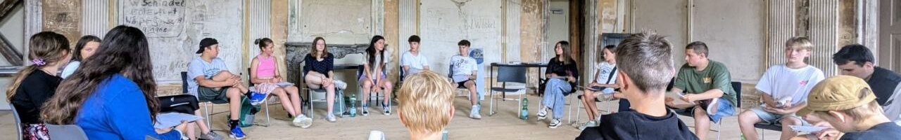 Die jungen Teilnehmenden sitzen in einem großen Stuhlkreis in einem Saal im Schloss Schwarzburg und unterhalten sich.