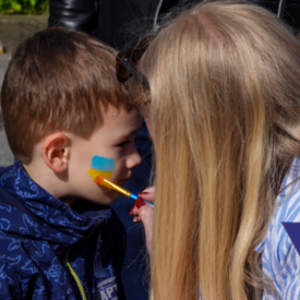 Ein Frau malt beim Europafest der vhs Kleve einem Jungen mit Wasserfarben eine Ukraine-Flagge auf die Wange.