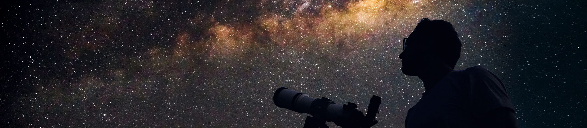 Eine Person steht vor einem Teleskop und blickt in den Sternenhimmel.