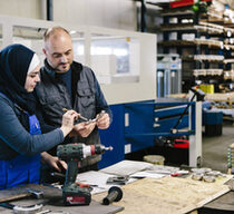 teamwork: technician explains a work tool to a young woman in a workshop