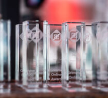 Viele Grimme Online Awards stehen auf einem Tisch. Das türkisblaue und rote Umgebungslicht bricht sich in den gläsernen Trophäen.