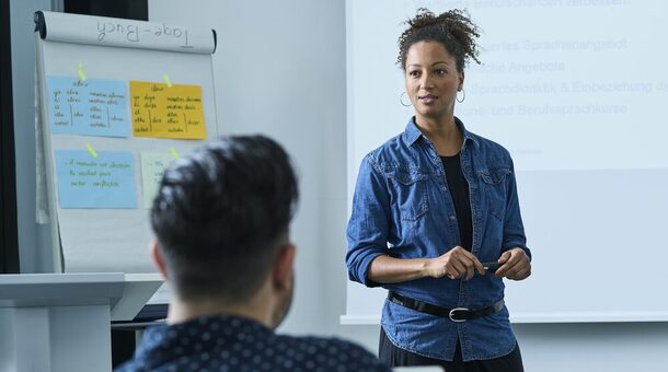 Eine junge Frau in einem Jeanshemd steht vor einer Klasse und unterrichtet