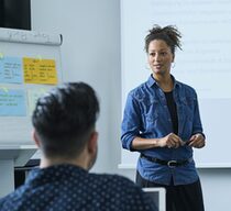 Eine junge Frau in einem Jeanshemd steht vor einer Klasse und unterrichtet