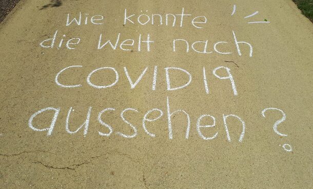Auf einer Straße steht mit Kreide geschrieben: Wie könnte eine Welt nach COVID19 aussehen?